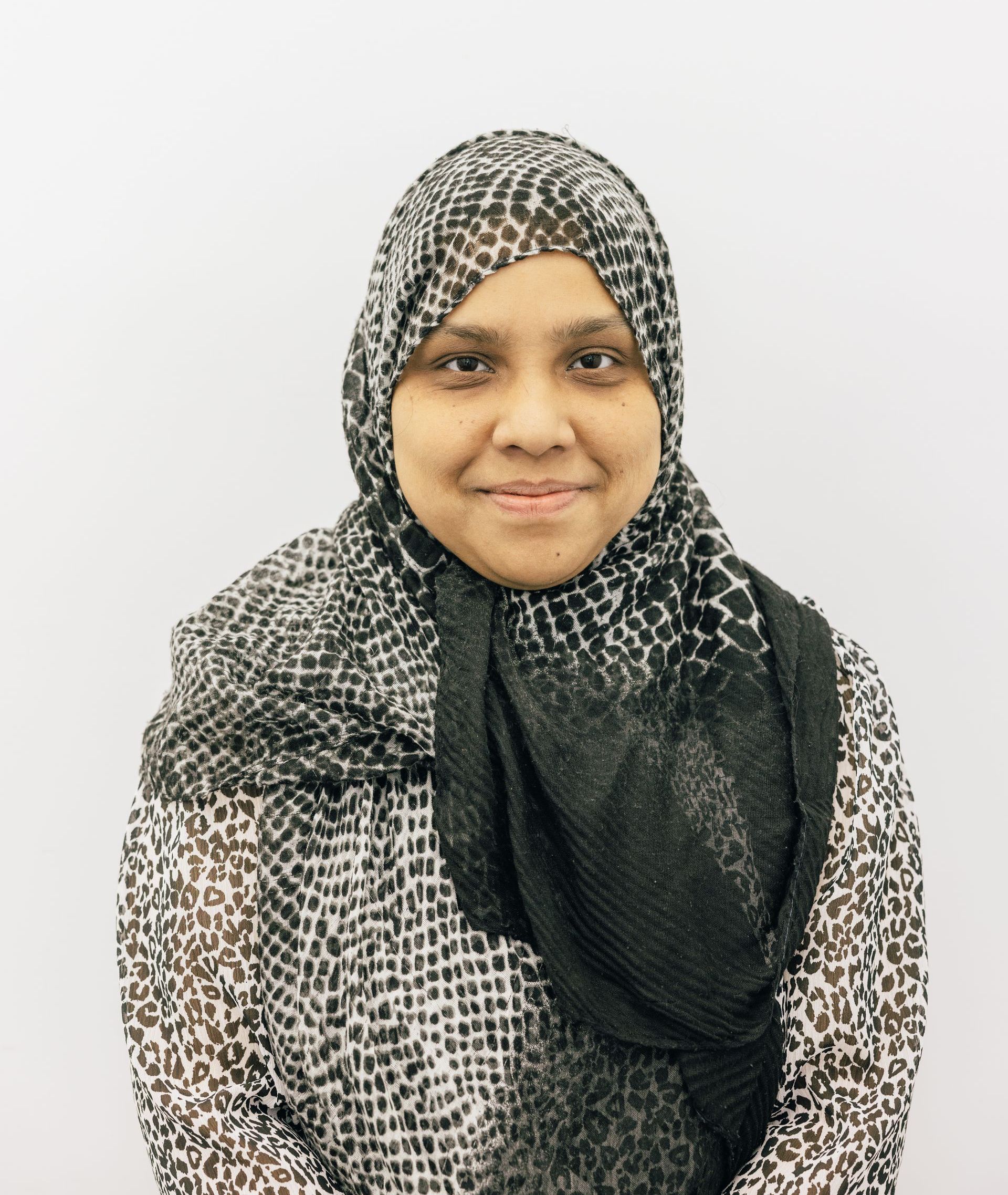 Person wearing a black-and-white patterned hijab, smiling against a plain light background