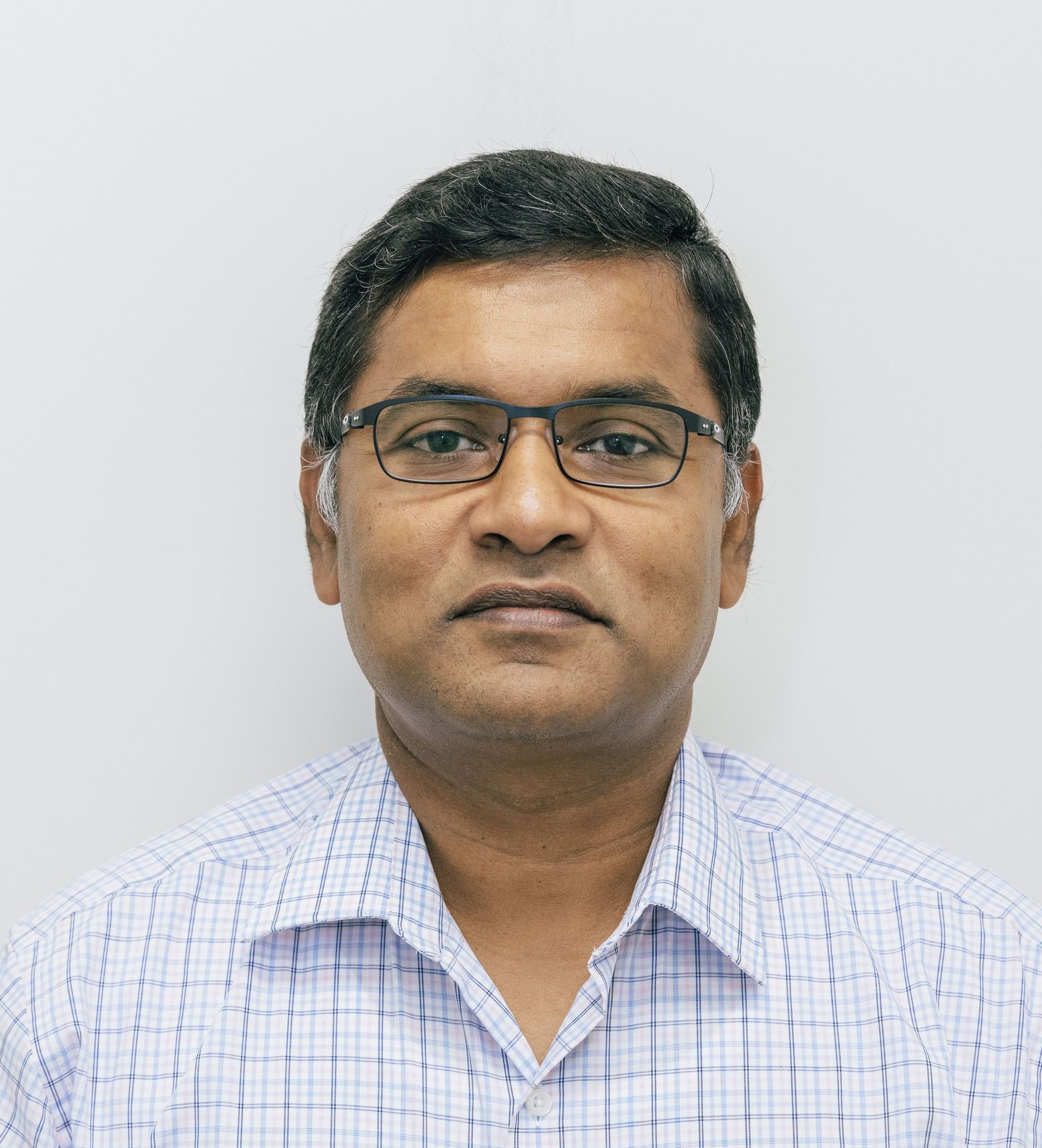 Portrait of a man wearing glasses and a light checkered shirt against a plain background