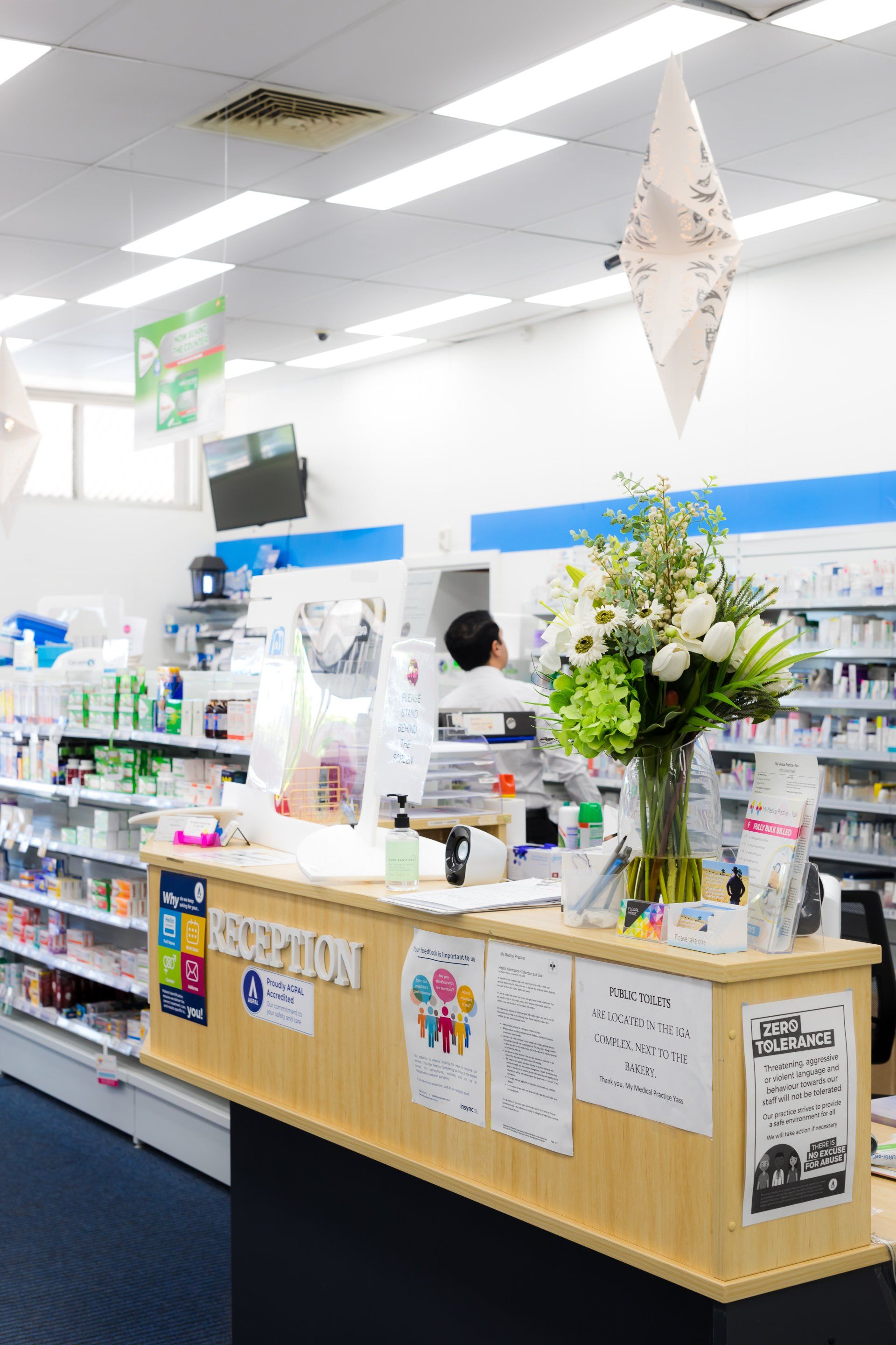 Pharmacy counter with flowers, product displays, and staff in a bright store interior