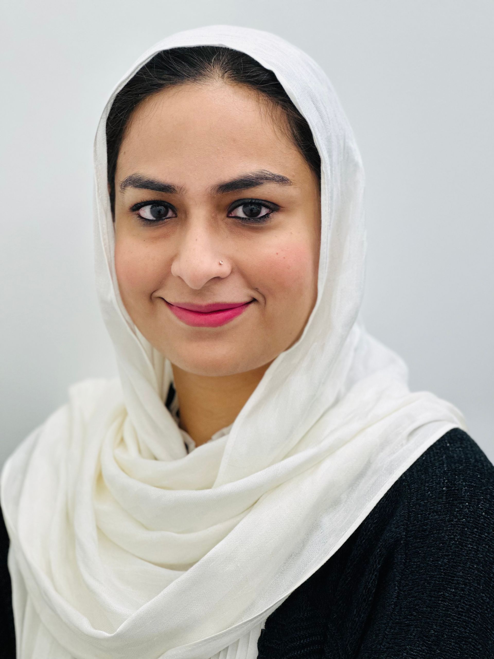 Portrait of a smiling person in a white headscarf and black top against a light background