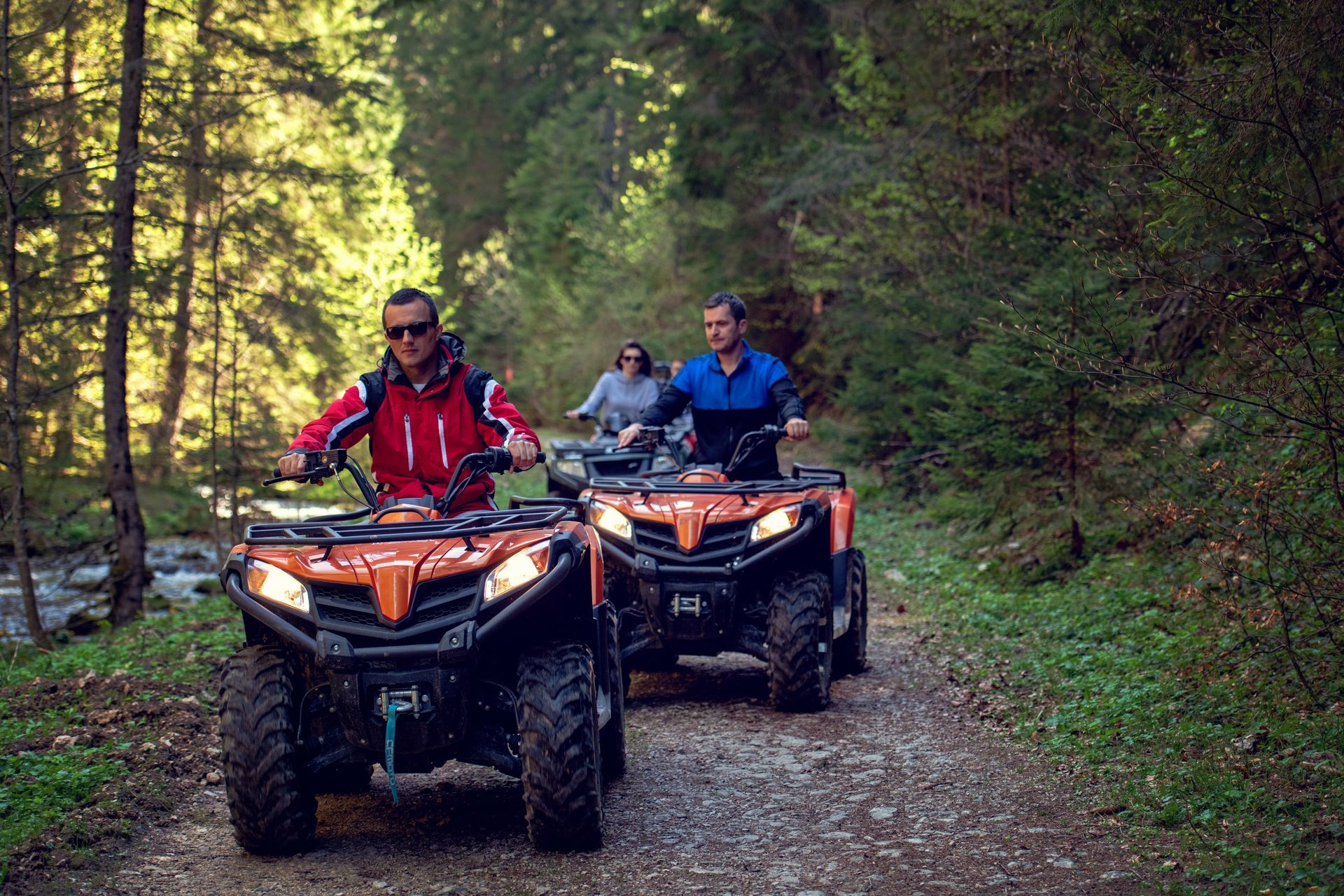 A group of people are riding atvs down a dirt road in the woods.