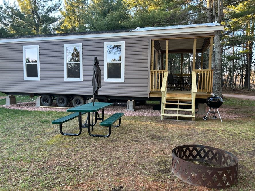 A mobile home with a picnic table and a fire pit in front of it.