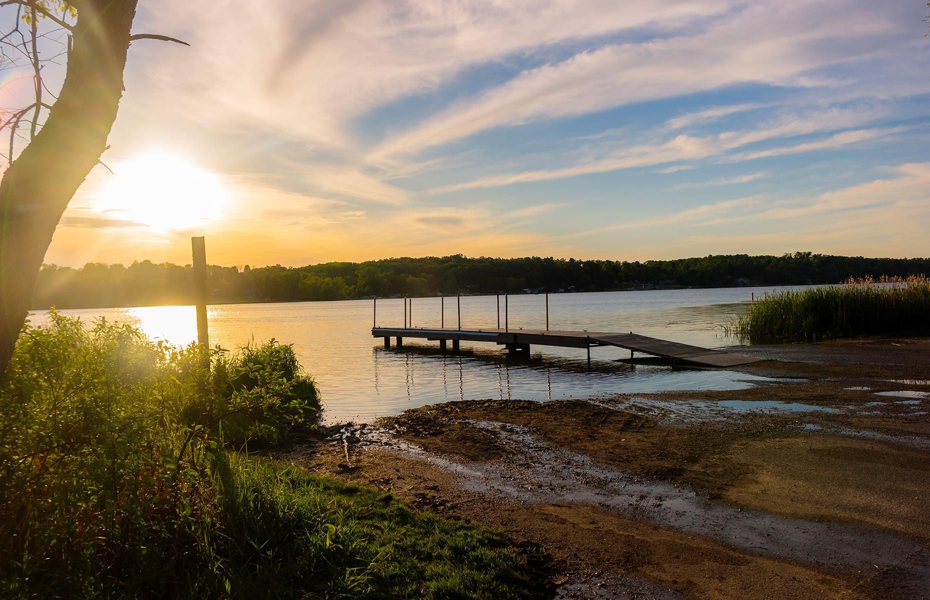 The sun is setting over a lake with a dock in the foreground.