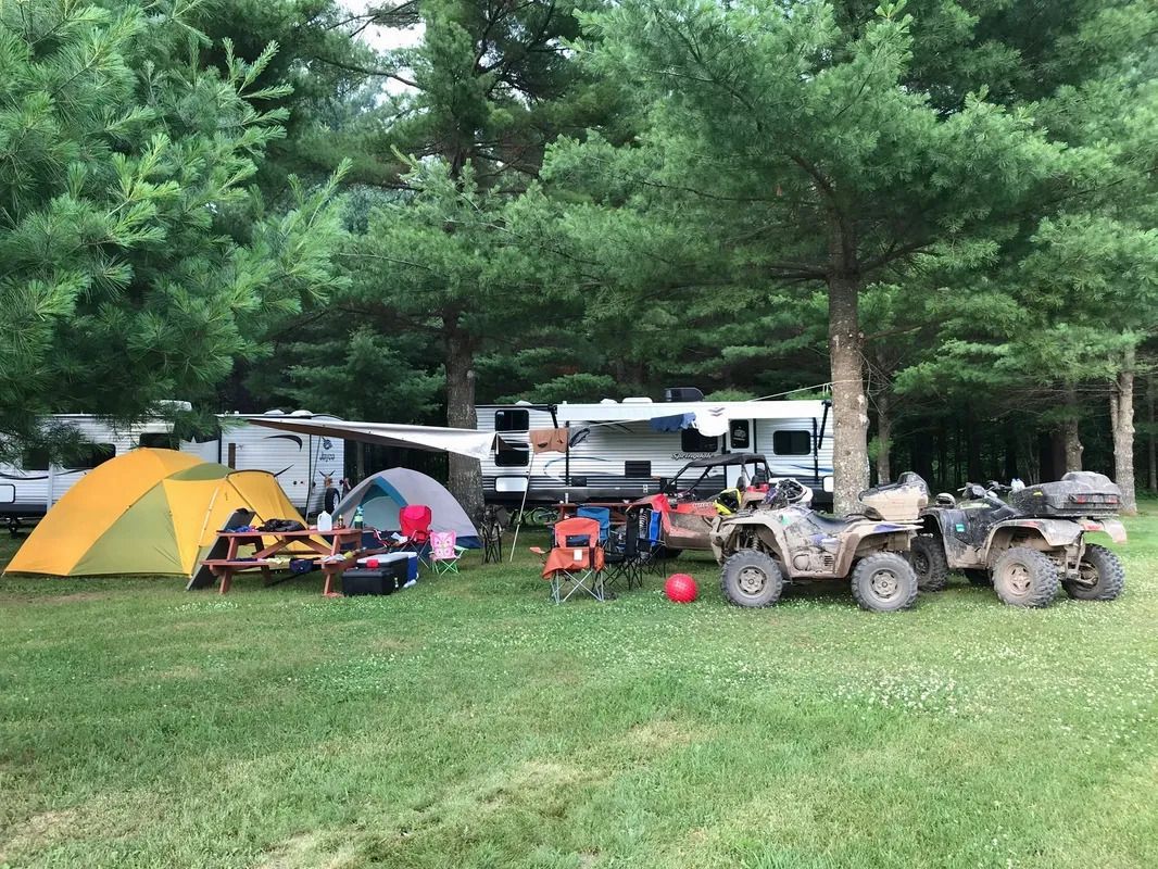 A group of people are camping in a field with tents and atvs.
