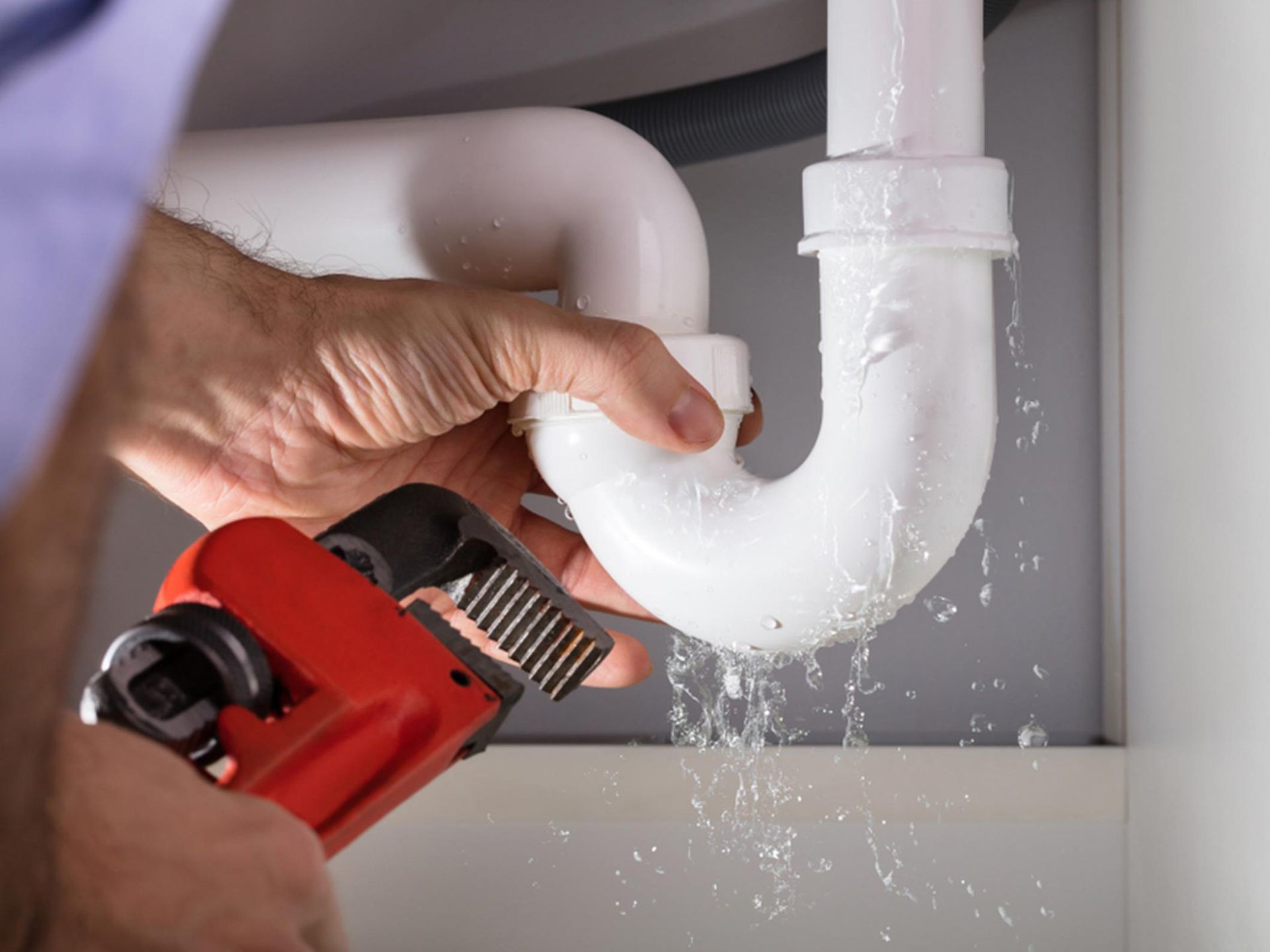 A plumber is fixing a leaking sink pipe with a wrench.