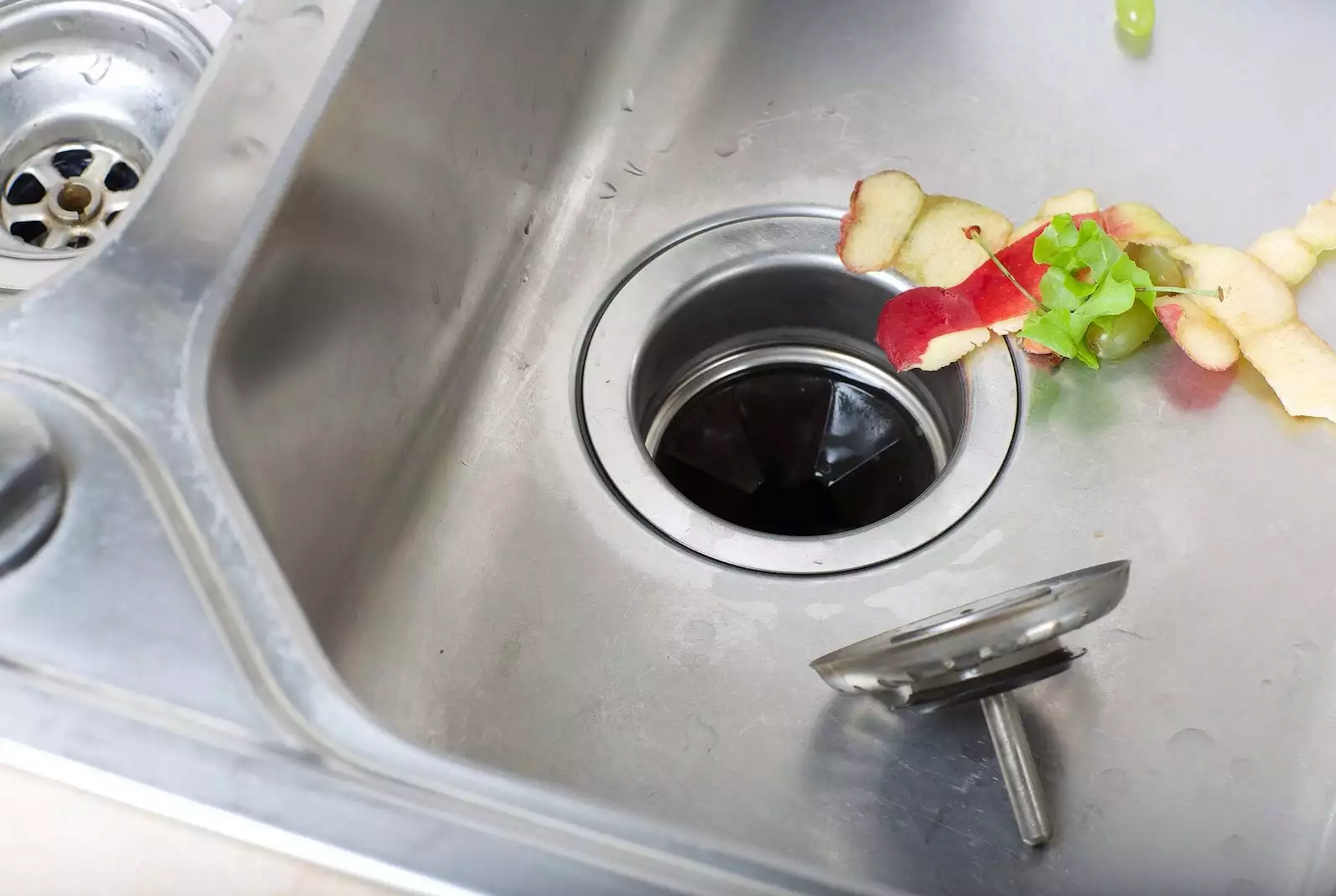 A stainless steel kitchen sink with food waste coming out of it.