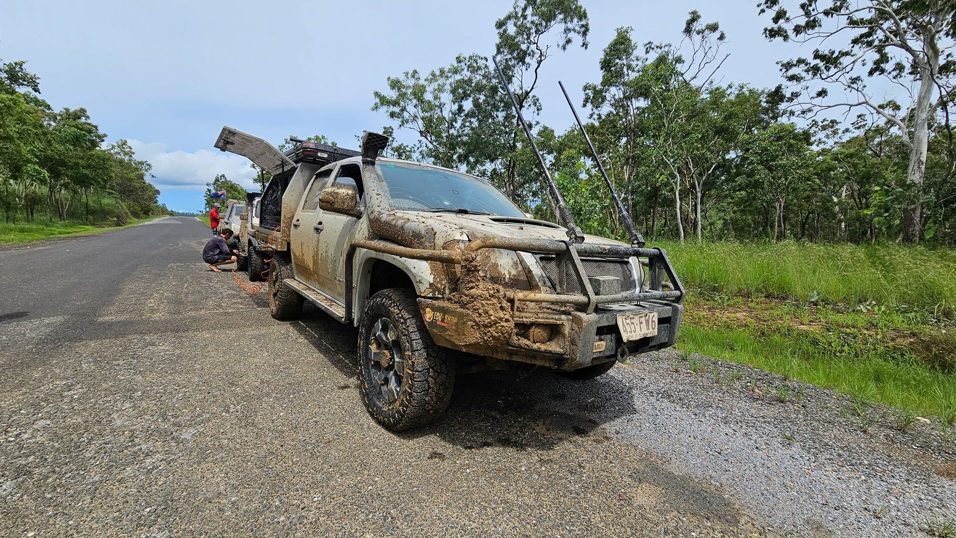 Mud-covered Off-road Vehicle On A Gravel Road, Partially Obscuring A Person. Trees And Sky In The Background — Track N Back 4x4 In Mareeba, QLD