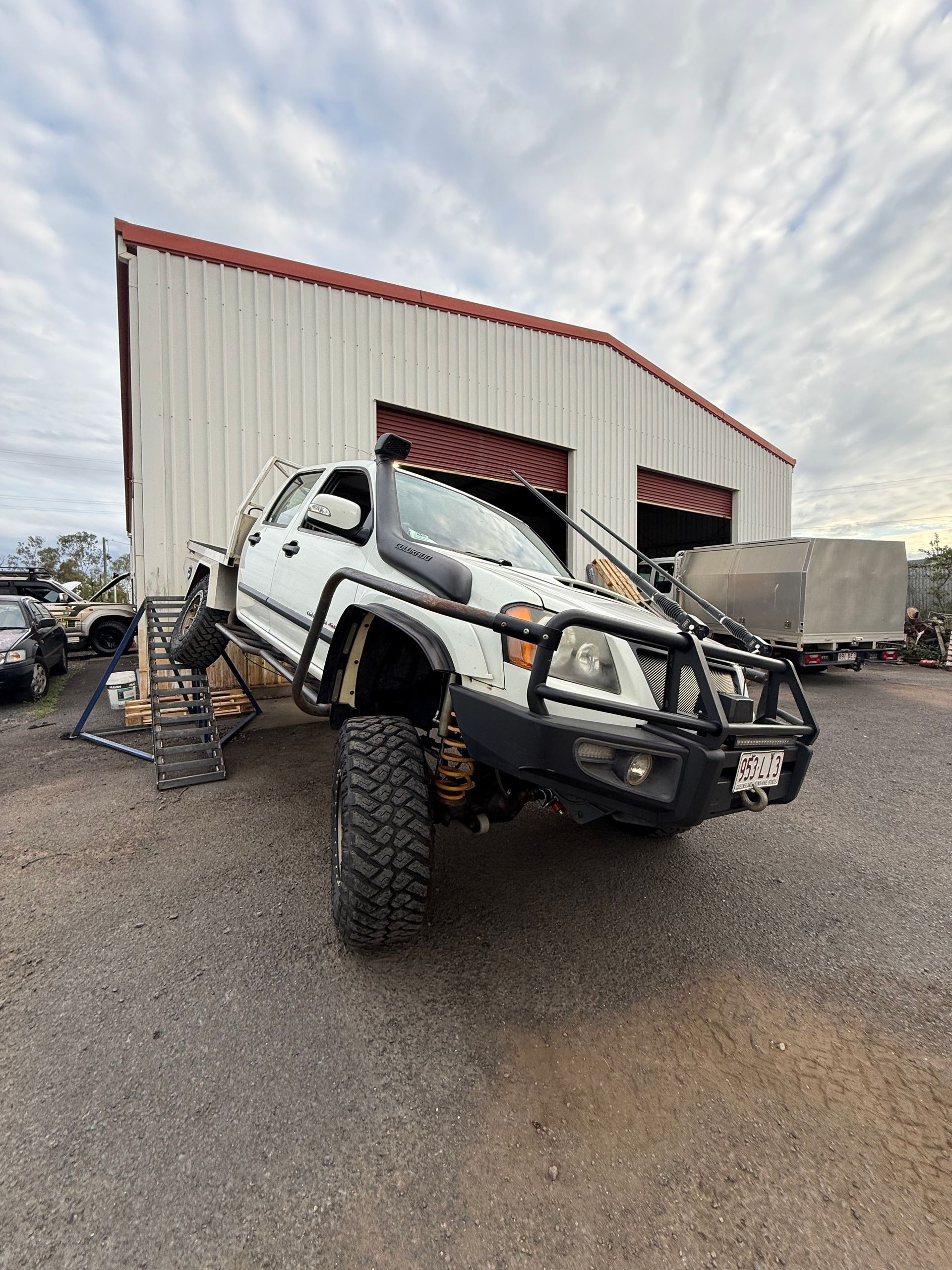 White Lifted Truck in Front of a Metal Building, One Tire Raised — Track N Back 4x4 In Mareeba, QLD
