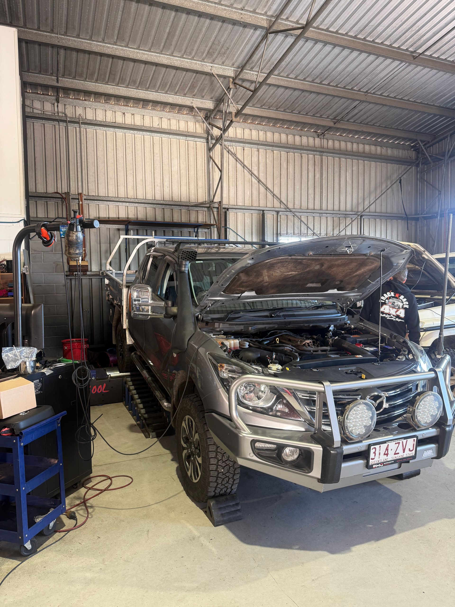 A pickup truck in a repair shop with its hood open; a mechanic is working — Track N Back 4x4 In Mareeba, QLD