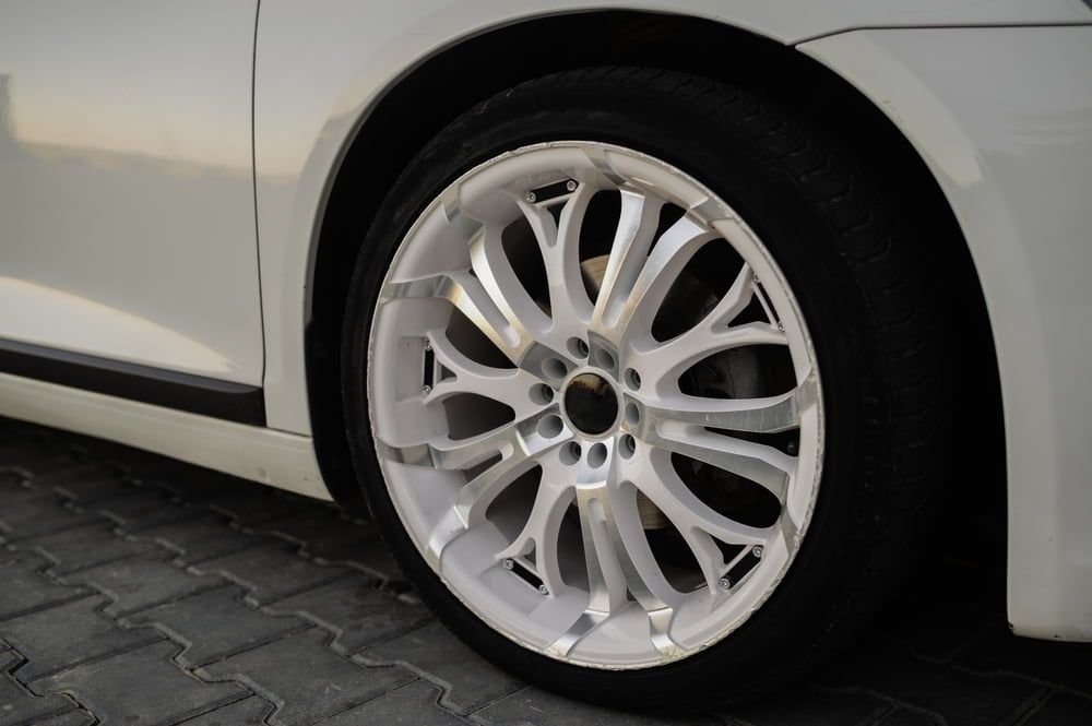 White Car Wheel With Silver Spokes on a Black Tire, Parked on Textured Pavement — Track N Back 4x4 In Townsville, QLD