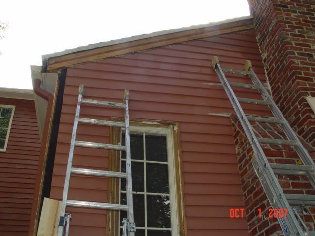 Two ladders leaning against a red house exterior near a brick chimney and window
