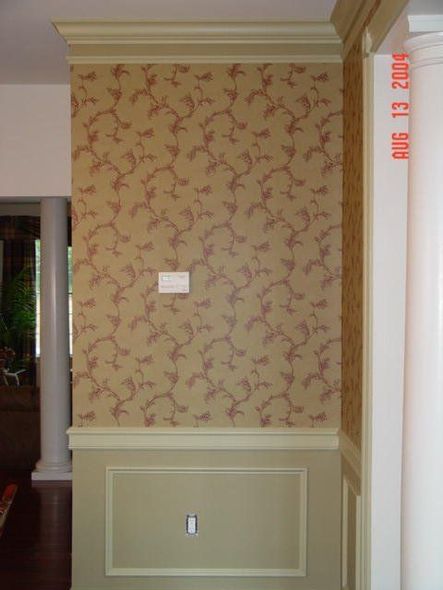 Interior wall with beige floral wallpaper, white trim, and a small wall plate in a hallway. Interior wall with beige floral wallpaper, white trim, and a small wall plate in a hallway.
