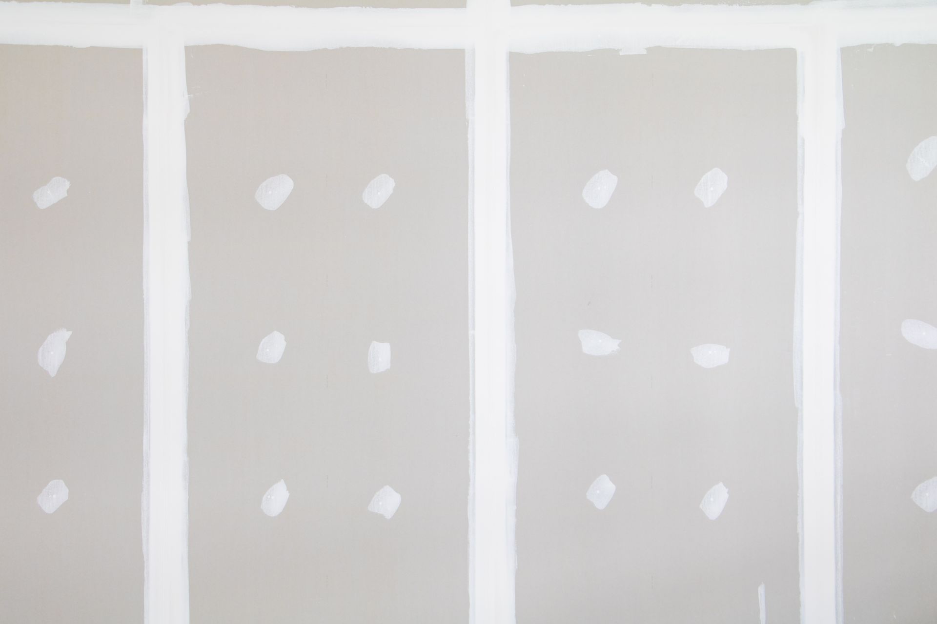 Unfinished drywall with white joint compound patches between vertical seams