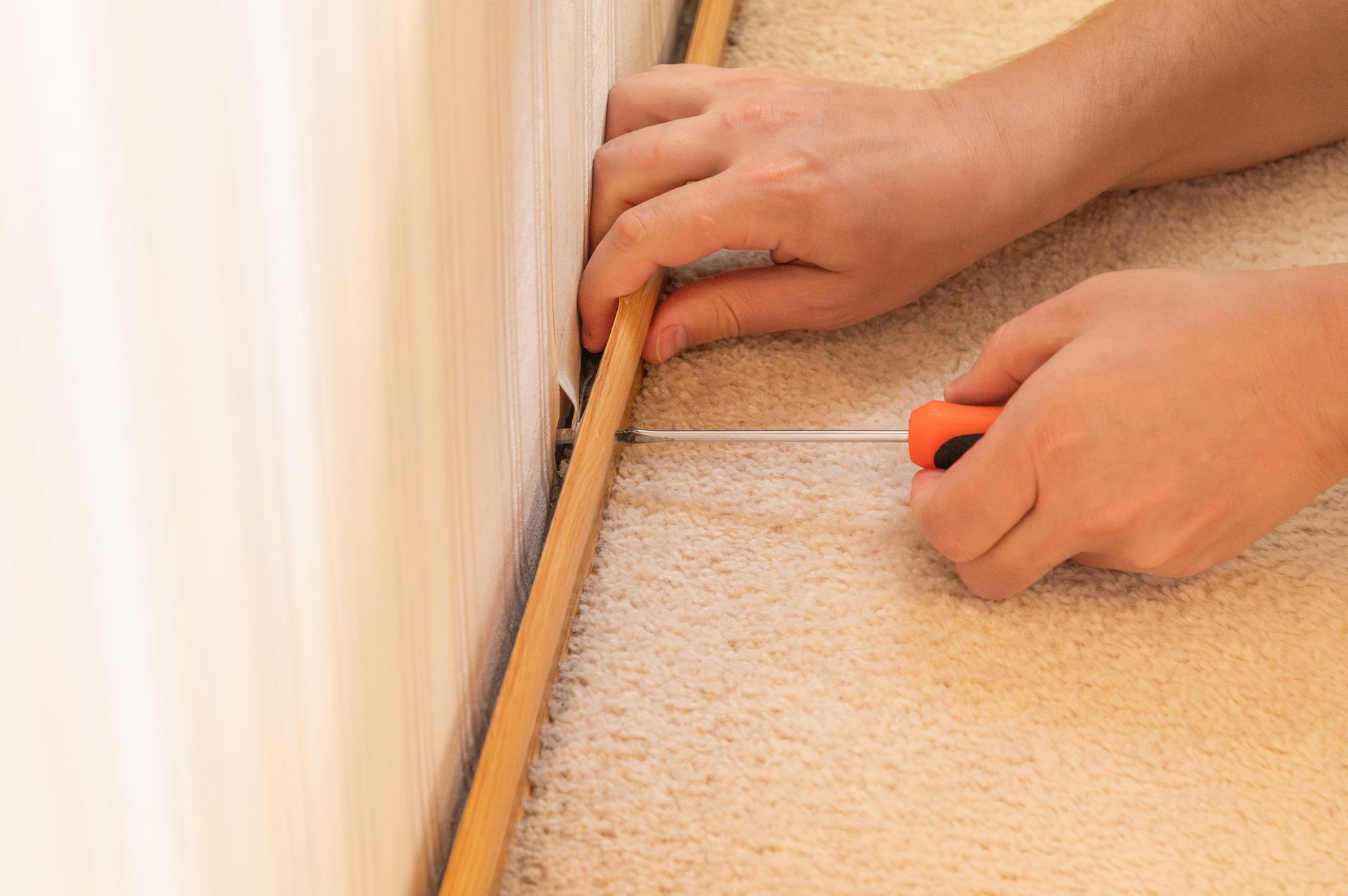 Hands measuring a baseboard with a tape measure along a wall and carpet edge. Hands measuring a baseboard with a tape measure along a wall and carpet edge.