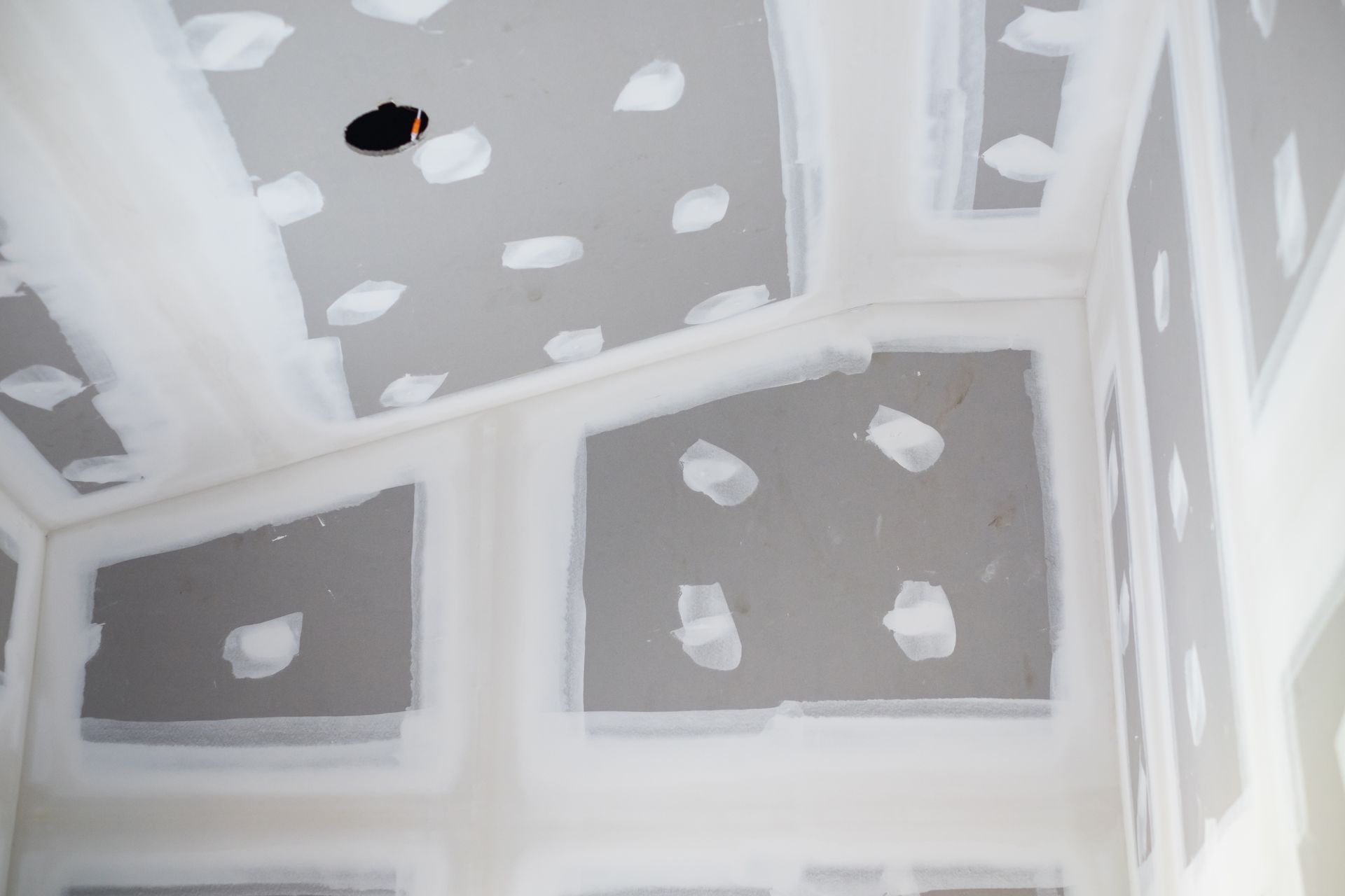 Unfinished drywall ceiling and walls with taped seams and gray patch spots in a small room