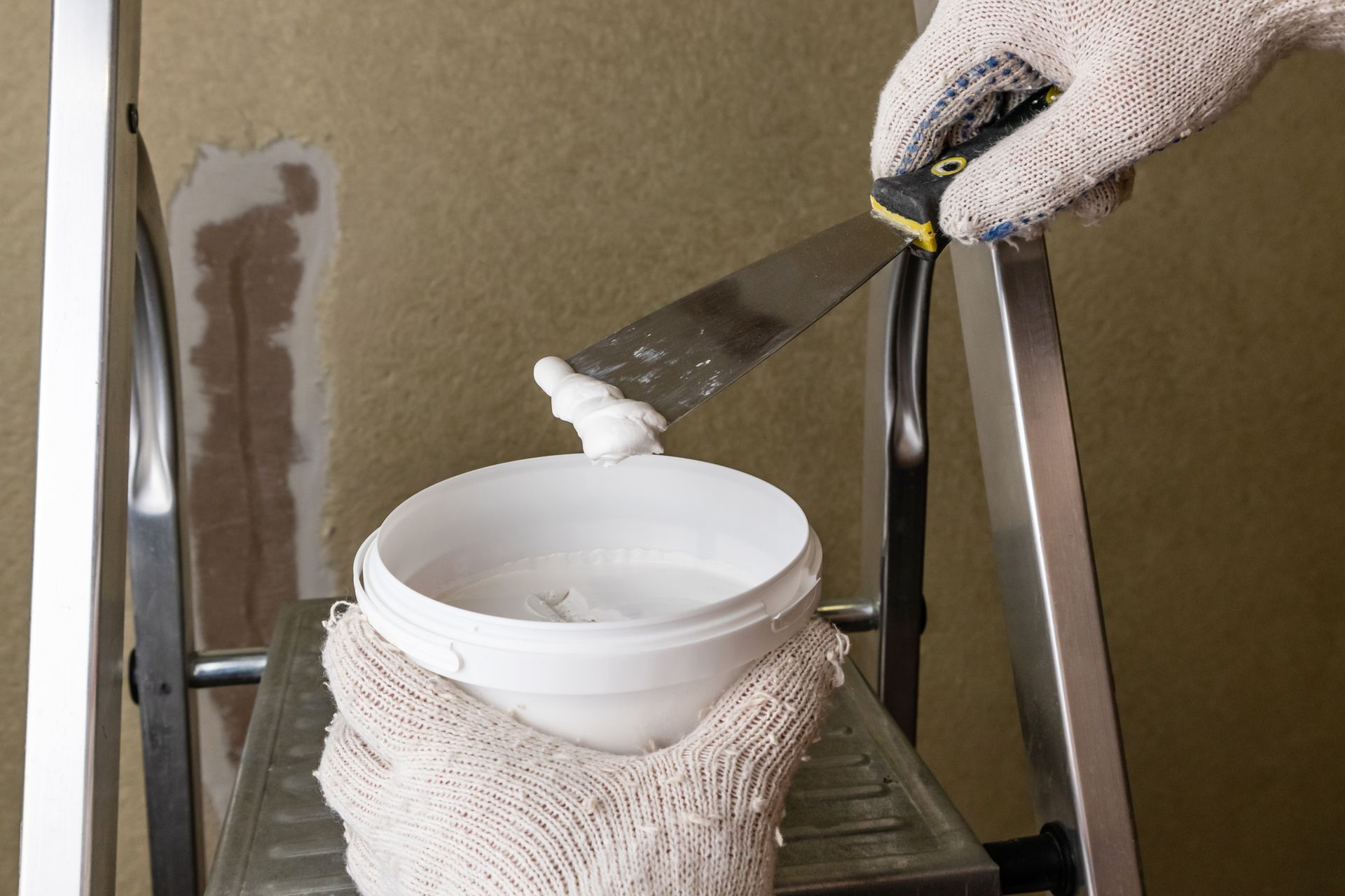 Gloved hands mixing white compound in a bucket during a wall repair Gloved hands mixing white compound in a bucket during a wall repair