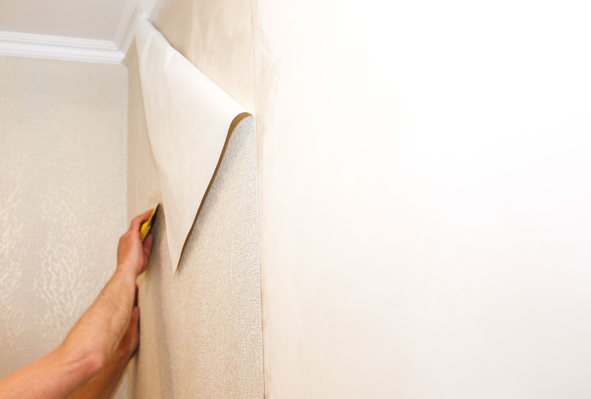A hand peeling back textured wallpaper from a wall corner, revealing a white surface underneath A hand peeling back textured wallpaper from a wall corner, revealing a white surface underneath