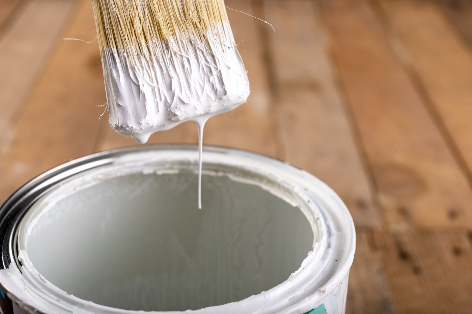 Paintbrush dripping white paint into an open can on a wooden floor. Paintbrush dripping white paint into an open can on a wooden floor.