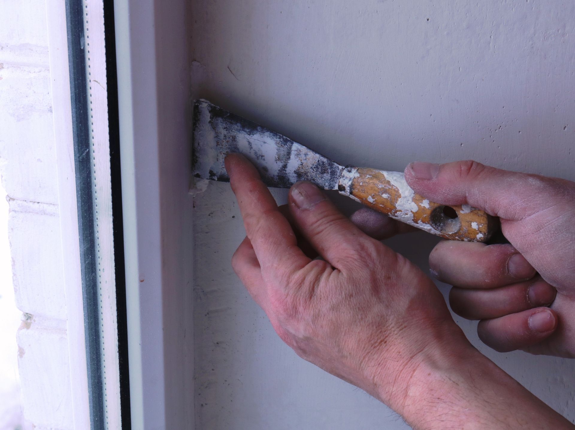 Hands scraping old paint from a wall corner with a putty knife Hands scraping old paint from a wall corner with a putty knife