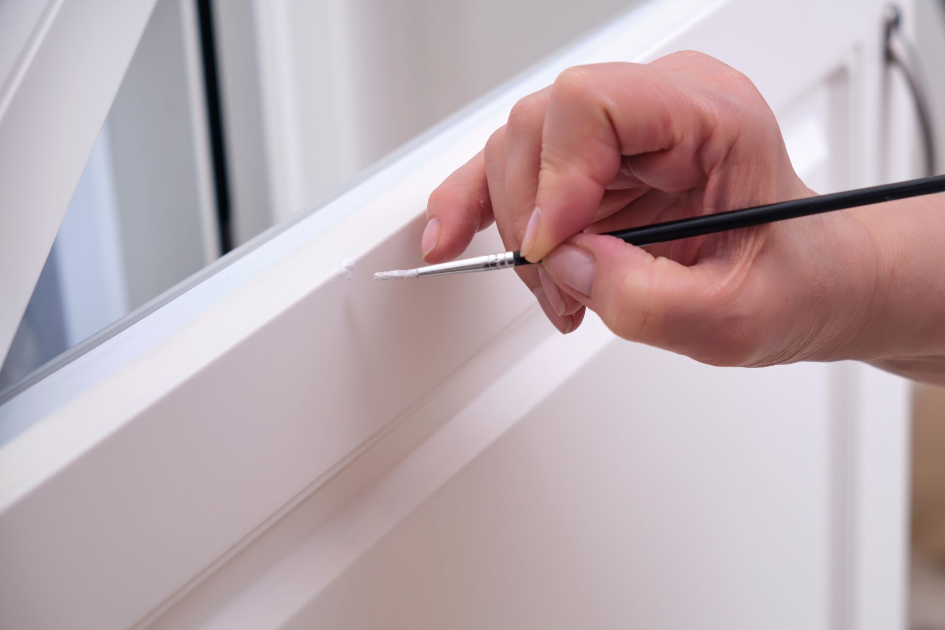 Hand painting a white window frame with a small brush Hand painting a white window frame with a small brush