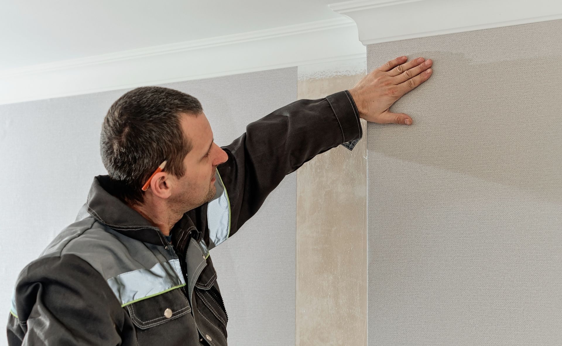 Man installing beige wallpaper on a wall, smoothing the edge with his hand Man installing beige wallpaper on a wall, smoothing the edge with his hand