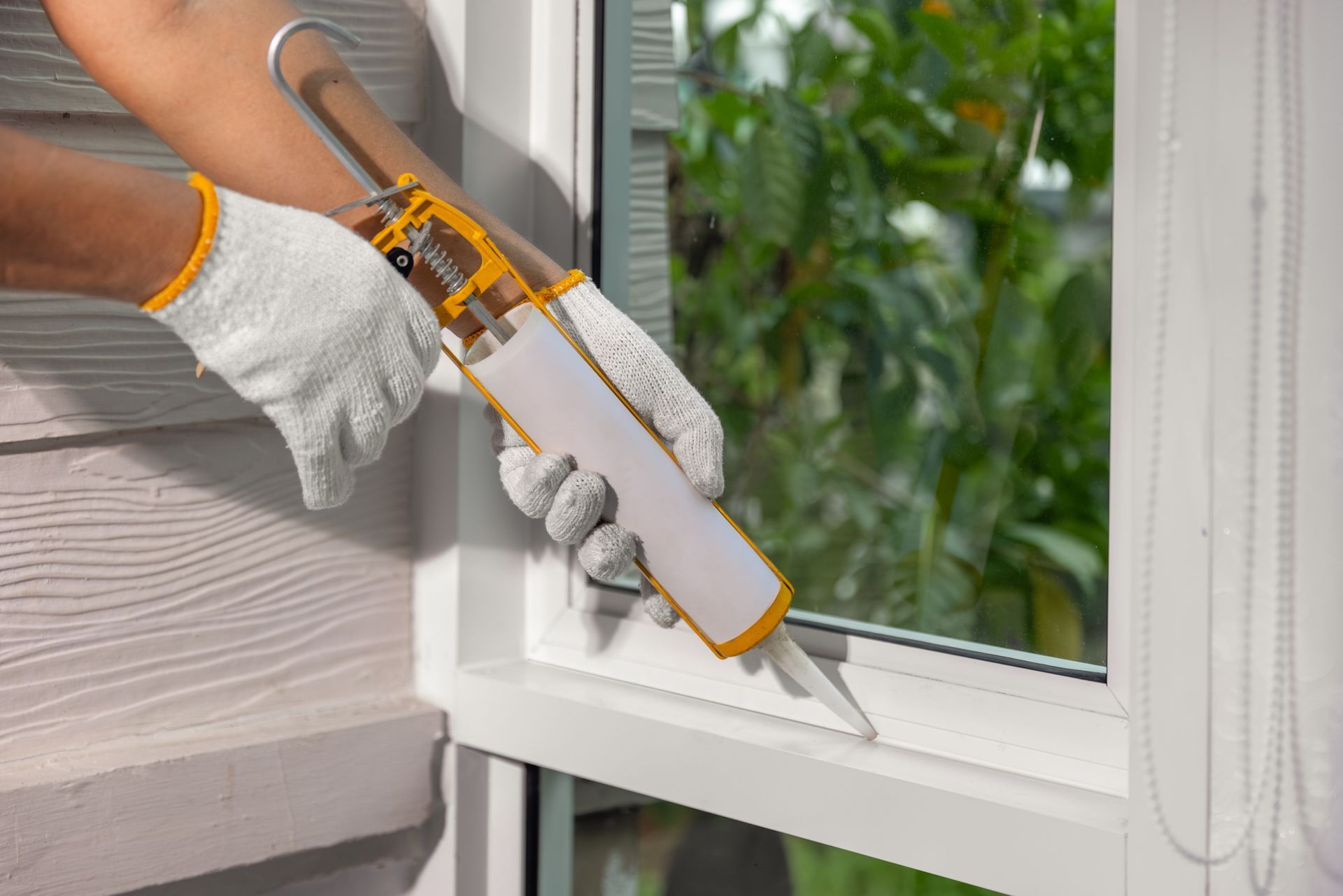 Gloved hands applying caulk around a white window frame with a caulking gun Gloved hands applying caulk around a white window frame with a caulking gun