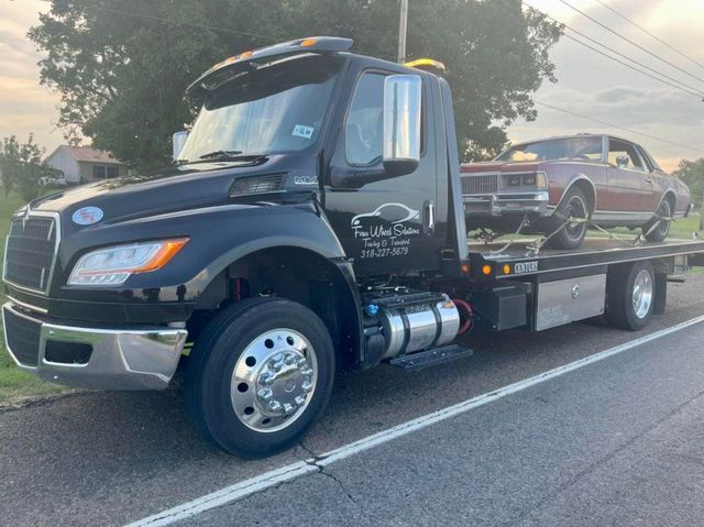 A black tow truck with a car on the back is parked on the side of the road.