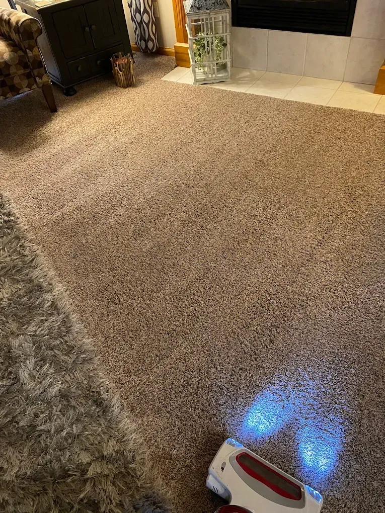 A vacuum cleaner with bright LED lights cleans a beige, textured carpet in a living room.