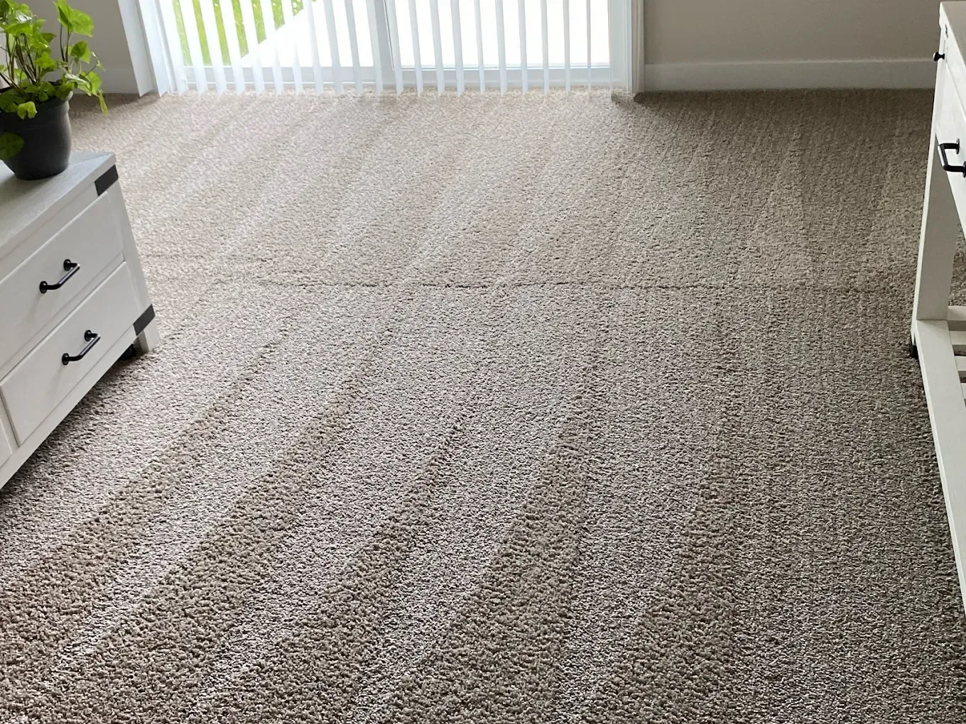 A room with neutral-toned, patterned wall-to-wall carpeting, flanked by two white pieces of furniture and a sliding door.