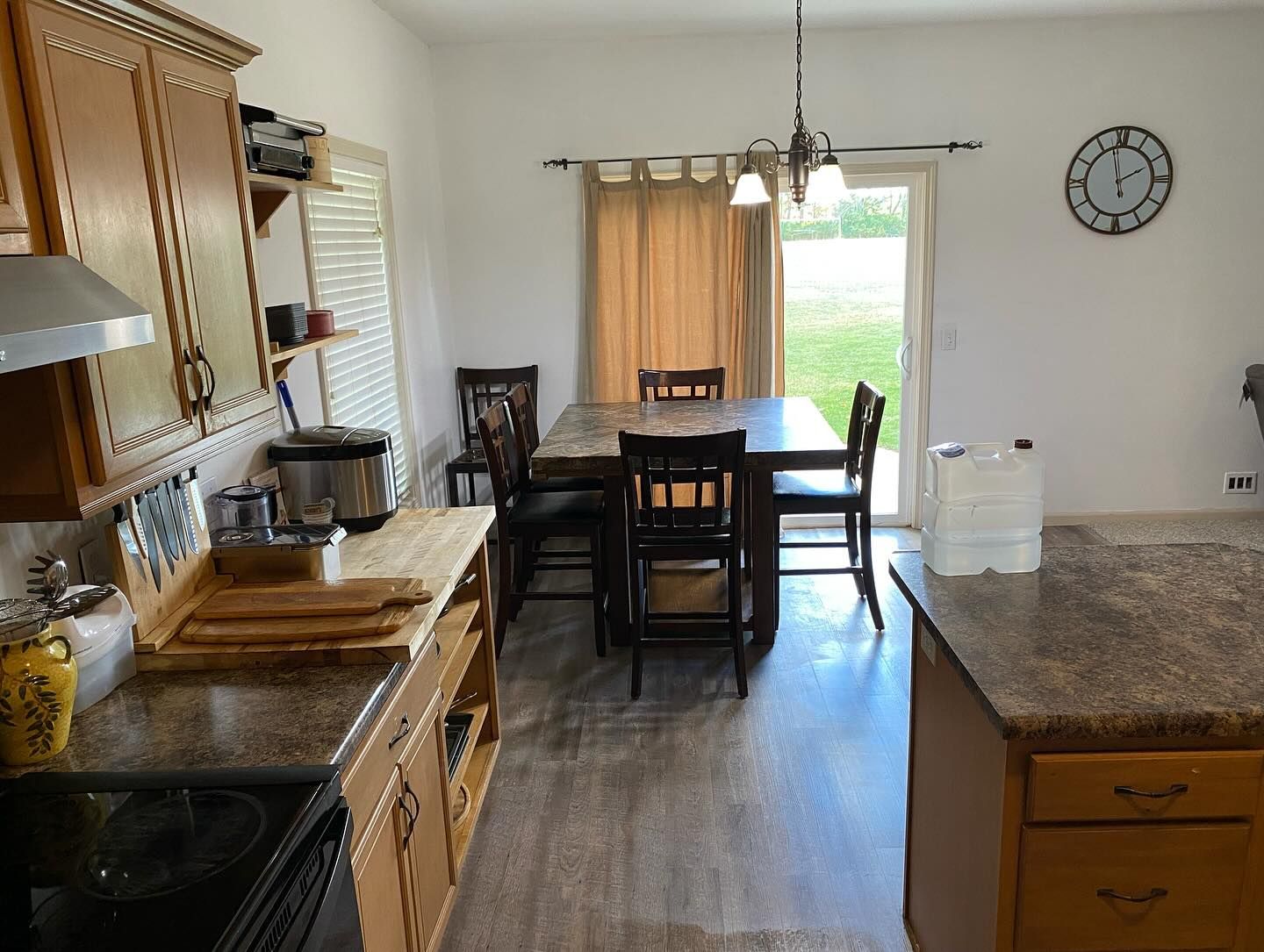 A kitchen with wooden cabinets, a granite-topped island, and a dining table set for four near a glass sliding door.