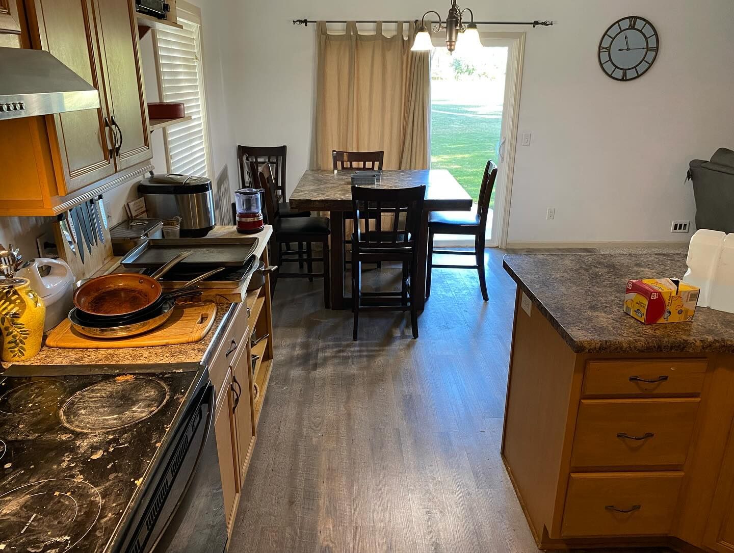 A kitchen featuring a dark wooden dining set, a stove with a messy surface, an island, and a clock on a white wall.