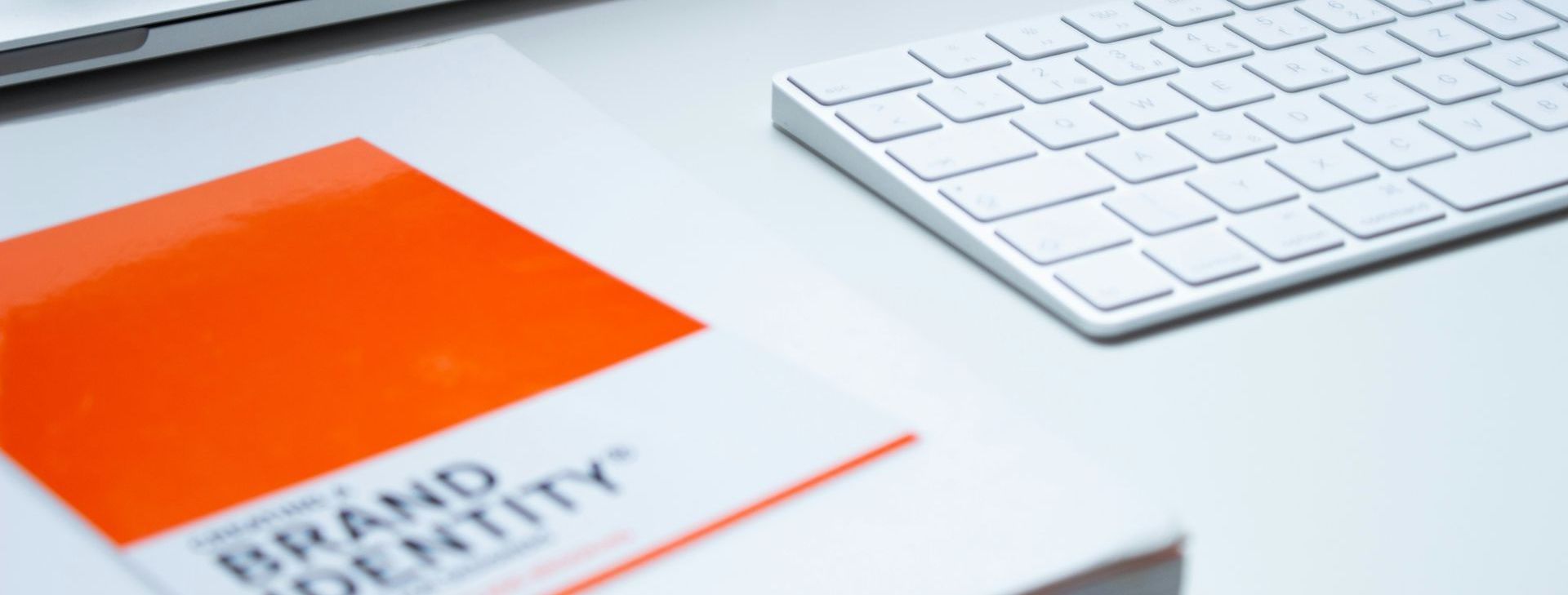 Un clavier blanc à côté d'un livret à la couverture orange vif. Le livret porte la mention « Identité de marque ».