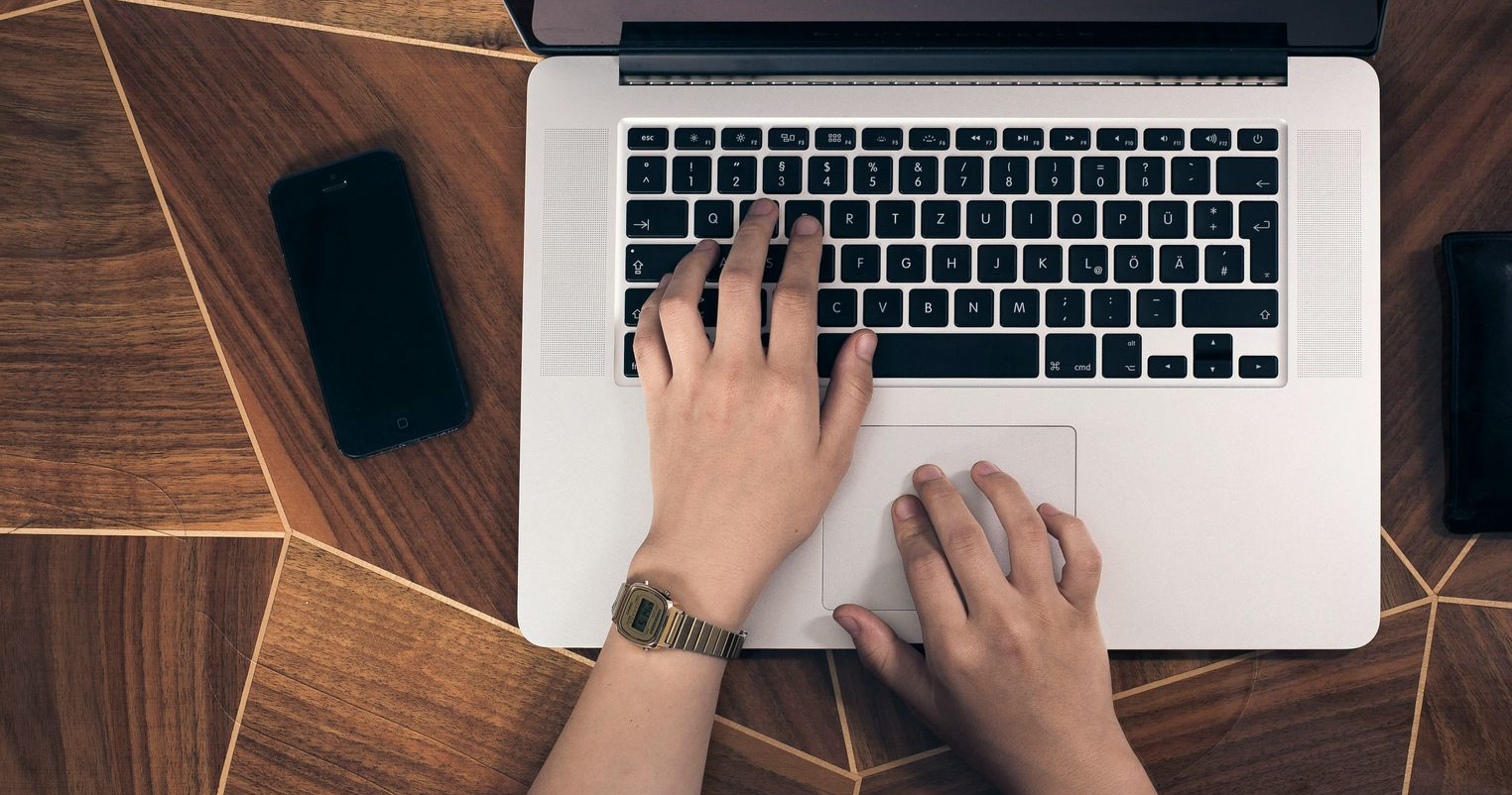 Personne tapant sur un ordinateur portable avec les mains sur le clavier et le trackpad. 
