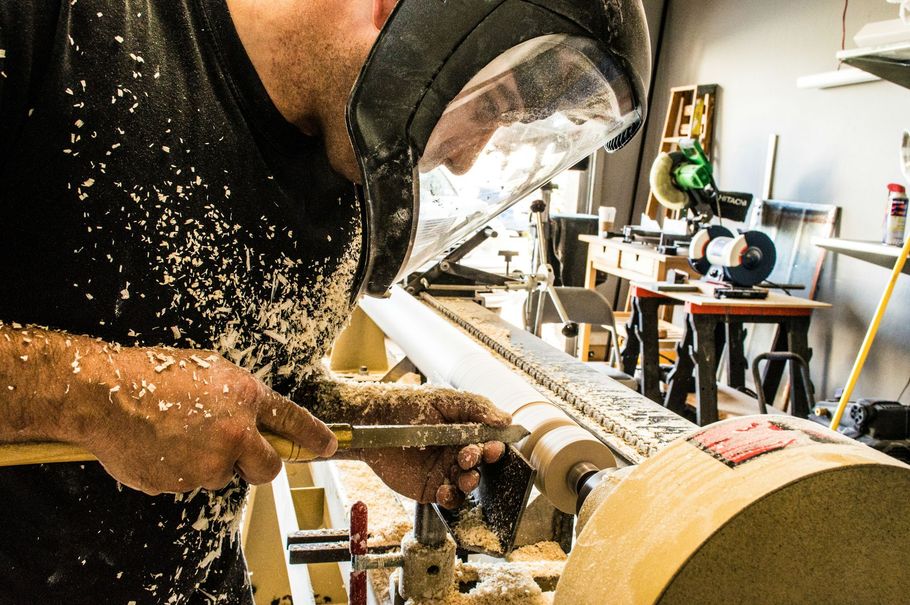 Woodworker sanding a wooden log on a lathe, with sawdust flying in a workshop.