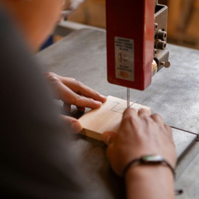 Hands guiding wood under a red band saw in a workshop