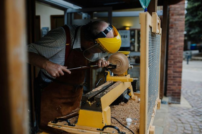 Person carving wood on a yellow lathe in a workshop doorway