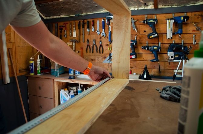 Person working on a wooden board in a workshop with tools hanging on the wall