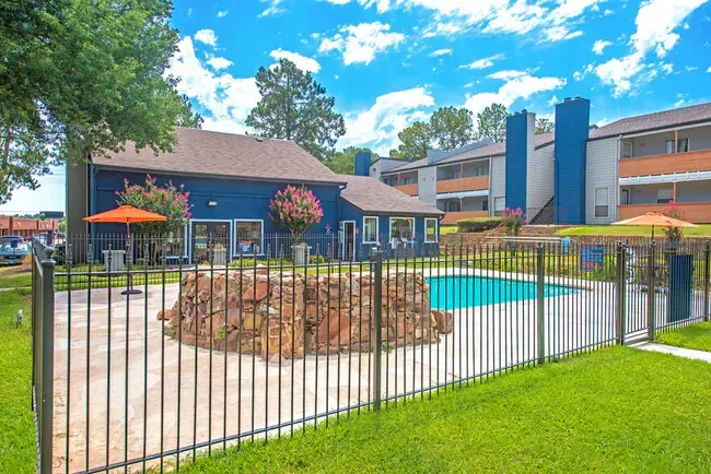 Pool area with blue buildings, sunny sky, and fenced-in pool.
