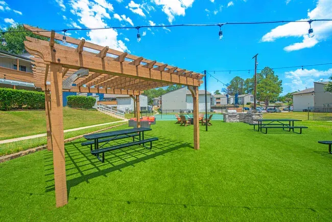 Outdoor recreation area with picnic tables, a wooden pergola, and string lights on a sunny day.