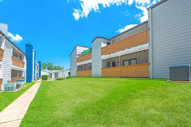 Apartment buildings with brown wooden balconies, green lawn, bright blue sky.