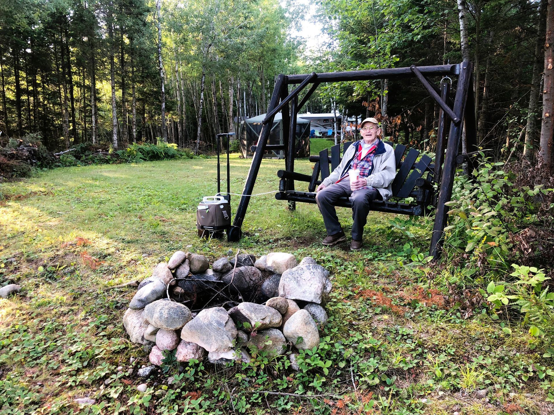 A man is sitting on a swing next to a fire pit.