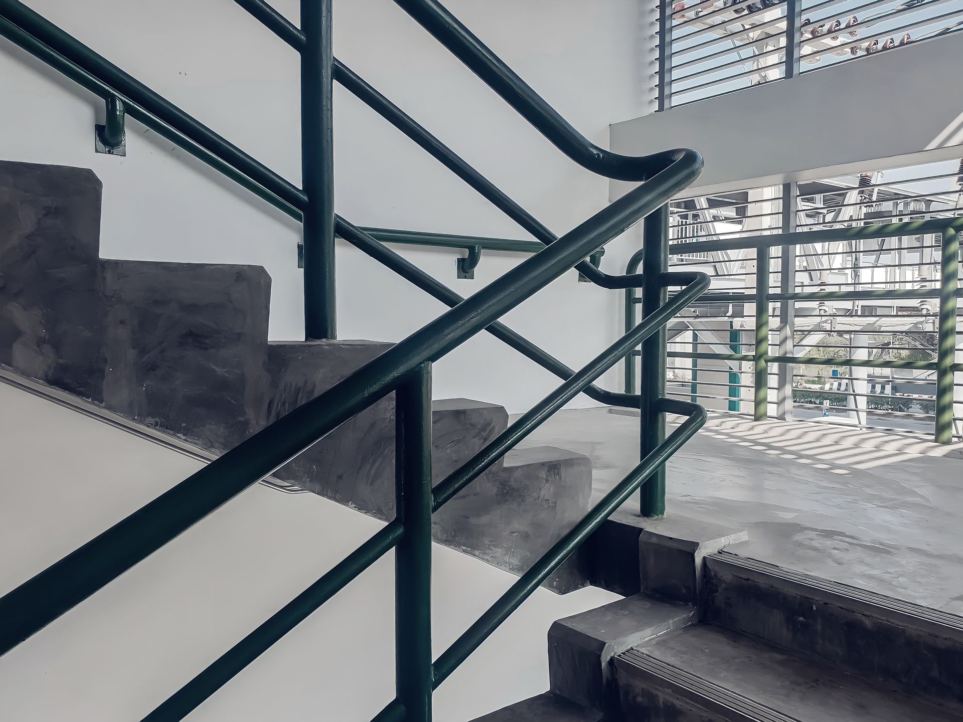 Modern stairwell with dark railings, gray steps, and large windows overlooking a building exterior