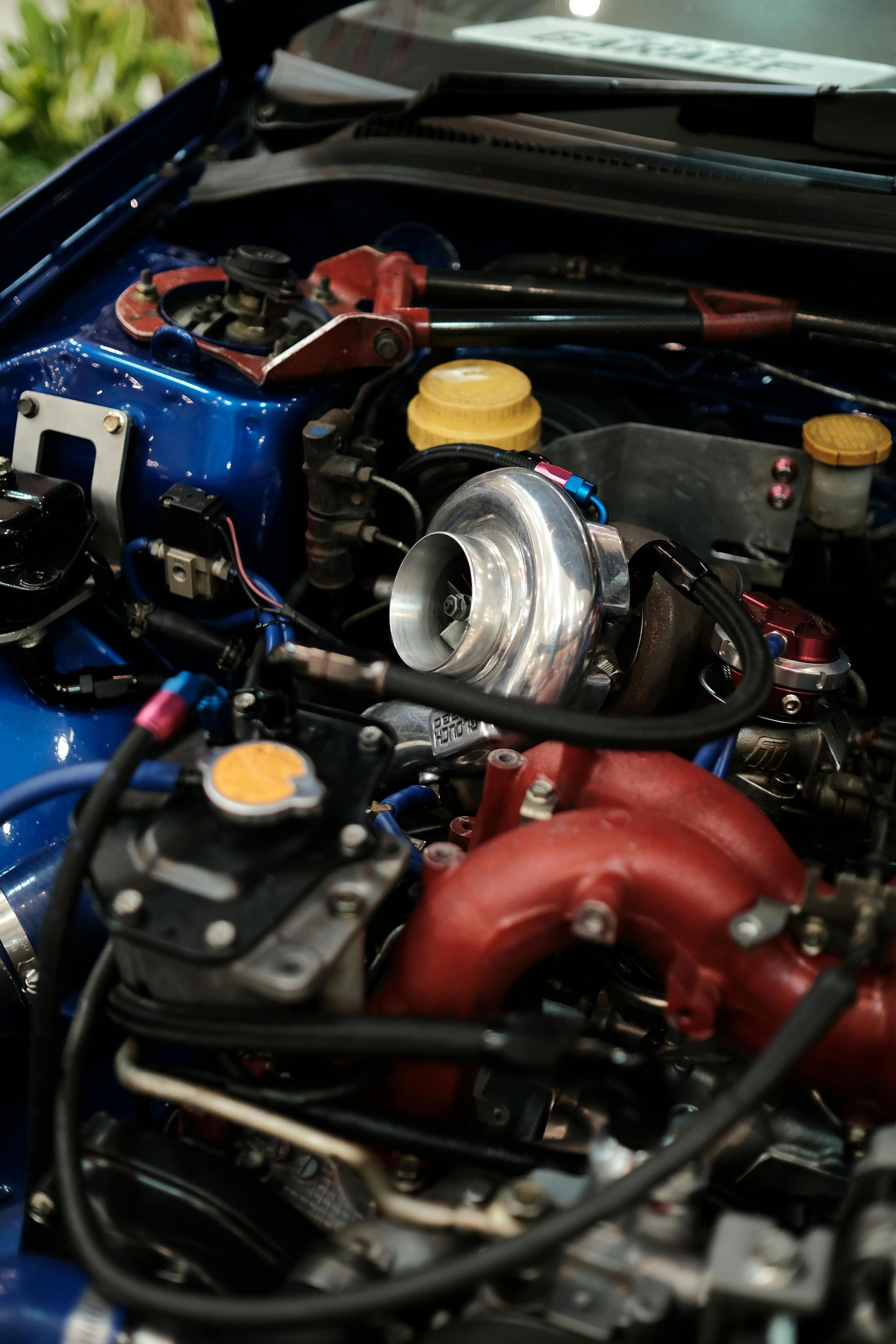 Car engine, silver and black components, various hoses and containers.