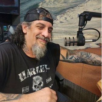 A man wearing a harley davidson shirt is sitting in front of a microphone.