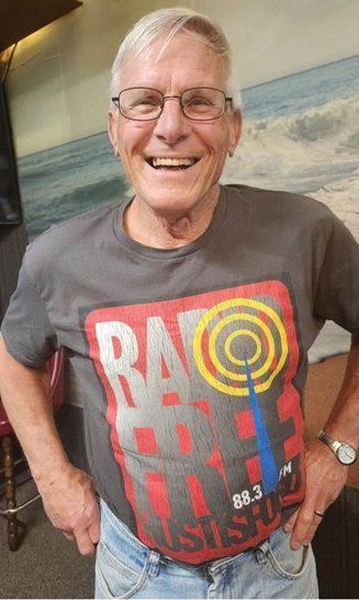 An older man wearing glasses and a t-shirt is smiling.