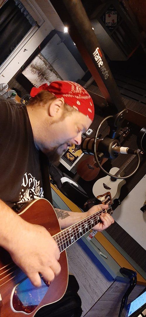 A man wearing a red bandana is playing an acoustic guitar.