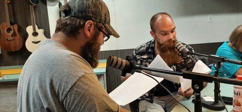 Two men are sitting in front of microphones in a room.
