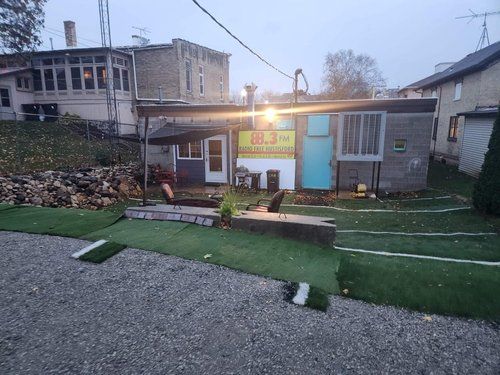 A small house is sitting on top of a gravel lot next to a building.