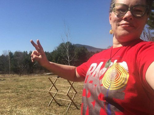 A woman in a red shirt is standing in a field giving a peace sign.