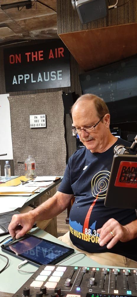 A man is sitting at a desk in front of a sign that says on the air applause.